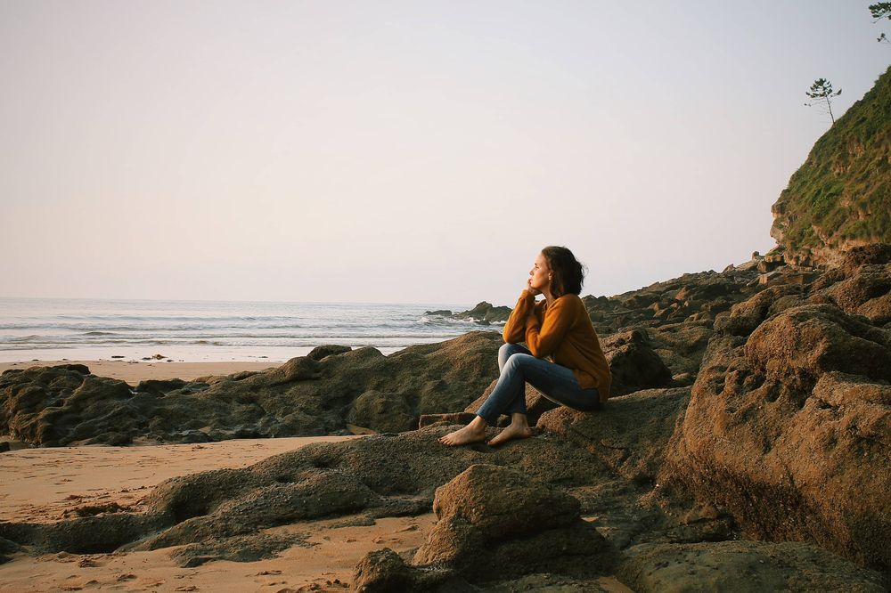 Una mujer sentada por la playa pensando