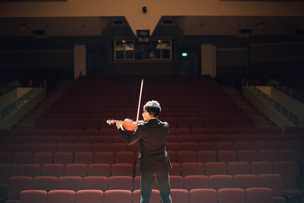 Hombre de pie frente a las butacas de un teatro tocando el violín
